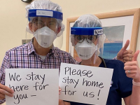 Two nurses wearing protective gear holding up signs.